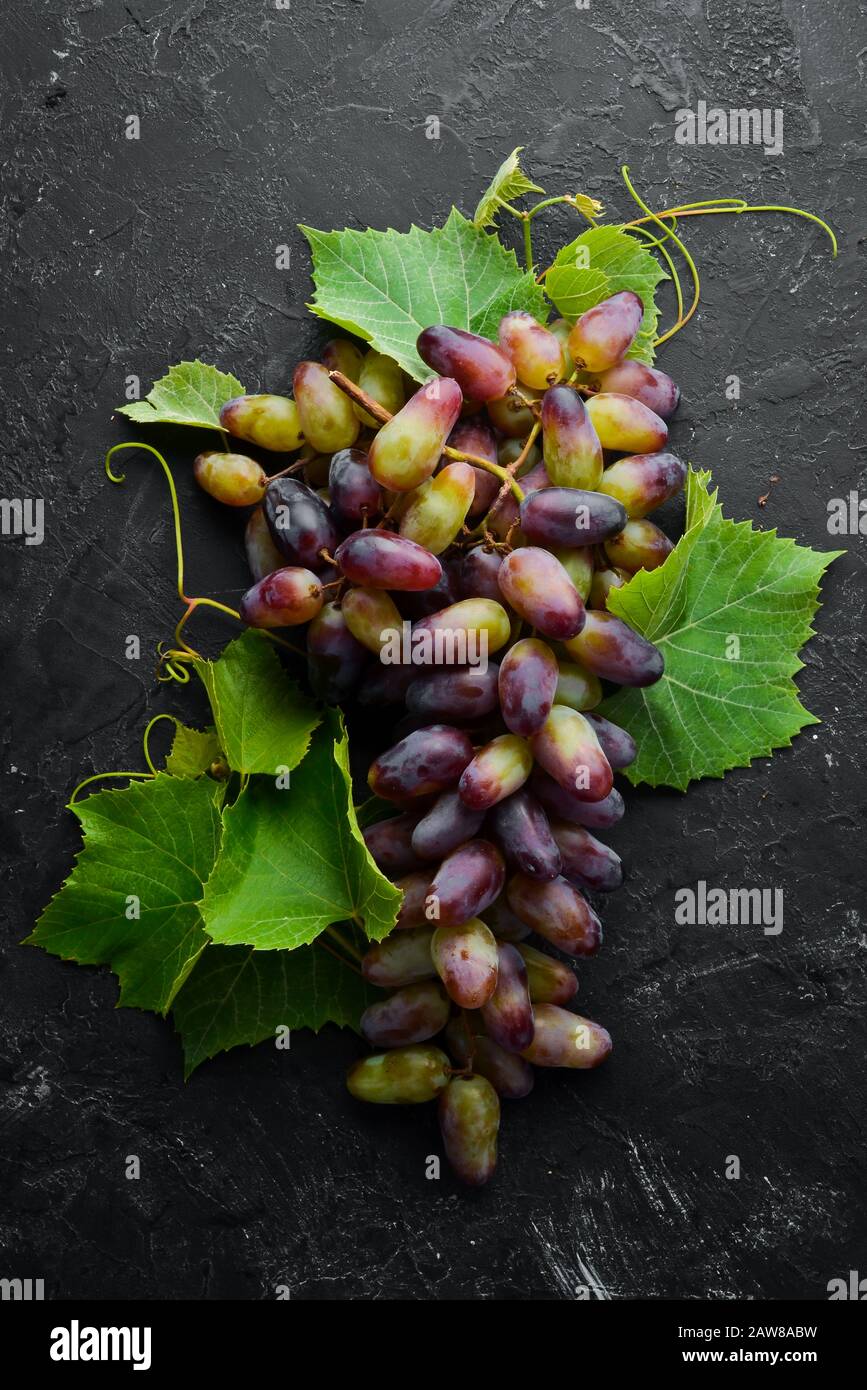 Fresh red grapes with leaves on a black stone table. Top view. Free space for your text. Stock Photo