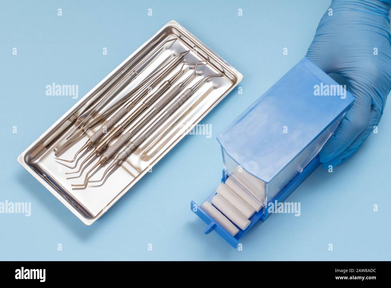 Dentist's hand in a latex glove with plastic box of cotton tampons, set of composite filling instruments for dental treatment in steel tray. Medical t Stock Photo