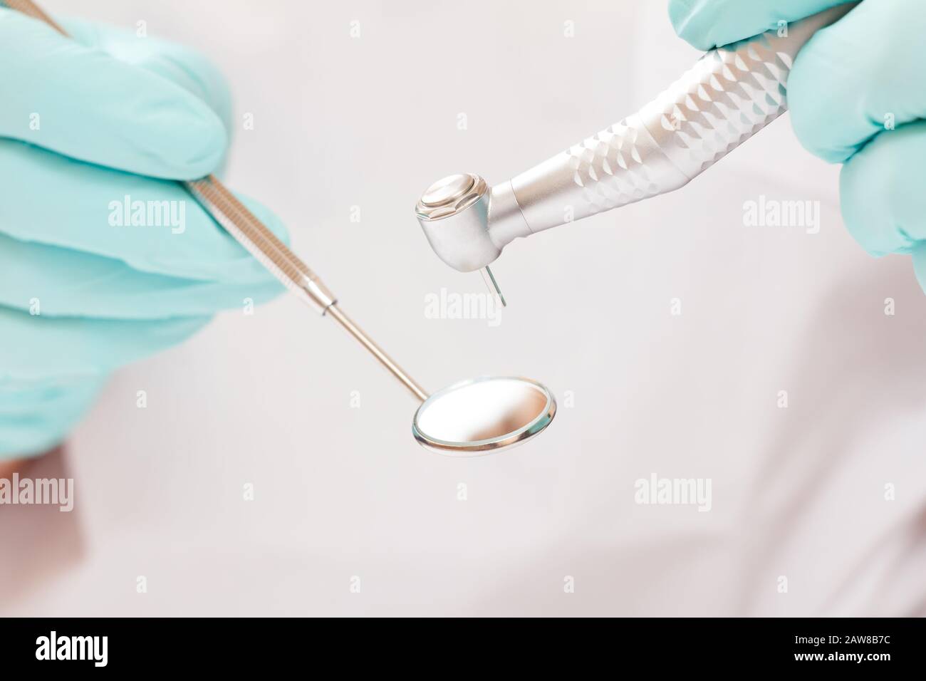 Close-up dentist's hands in latex gloves with mouth mirror and high-speed dental handpiece on blurred background. Medical tools concept. Shallow depth Stock Photo
