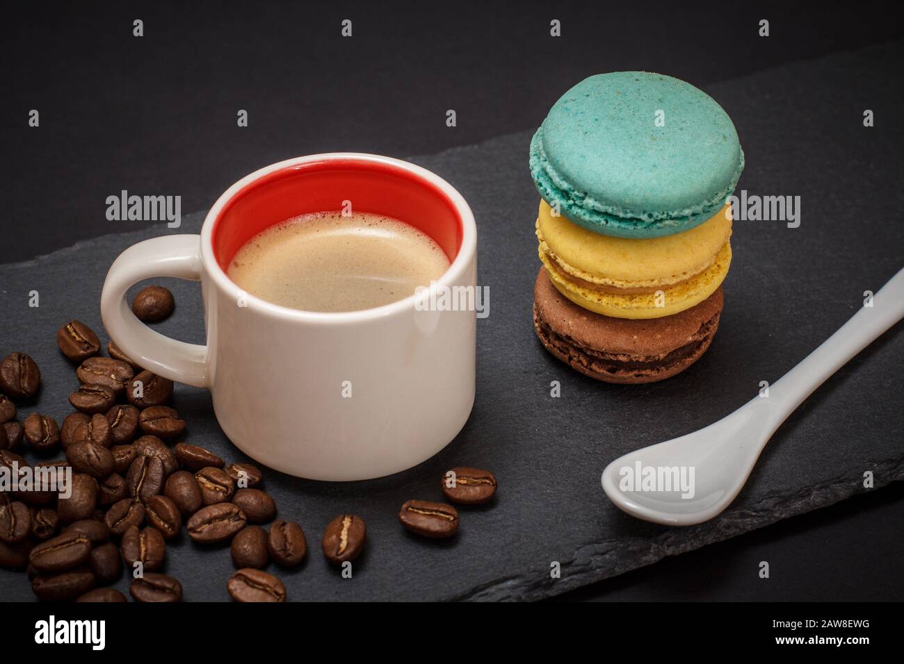 Cup of coffee, coffee beans, macaroons and spoon on black background. Top view. Stock Photo