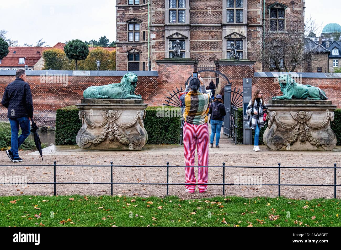 Hvilende loever, Two Resting Lions. Bronze sculptures in the King’s Garden at Rosenborg Castle, Copenhagen, Denmark. Woman tourist taking photo Stock Photo