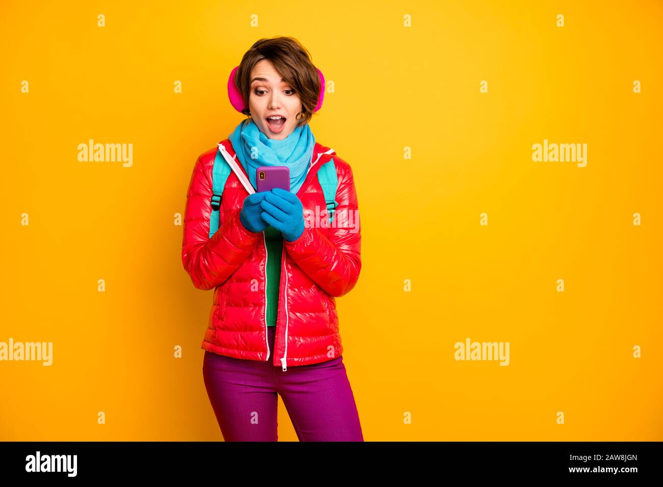 Photo of funny blogger lady look telephone screen read positive comments likes wear casual red coat blue scarf gloves ear covers pants isolated yellow Stock Photo