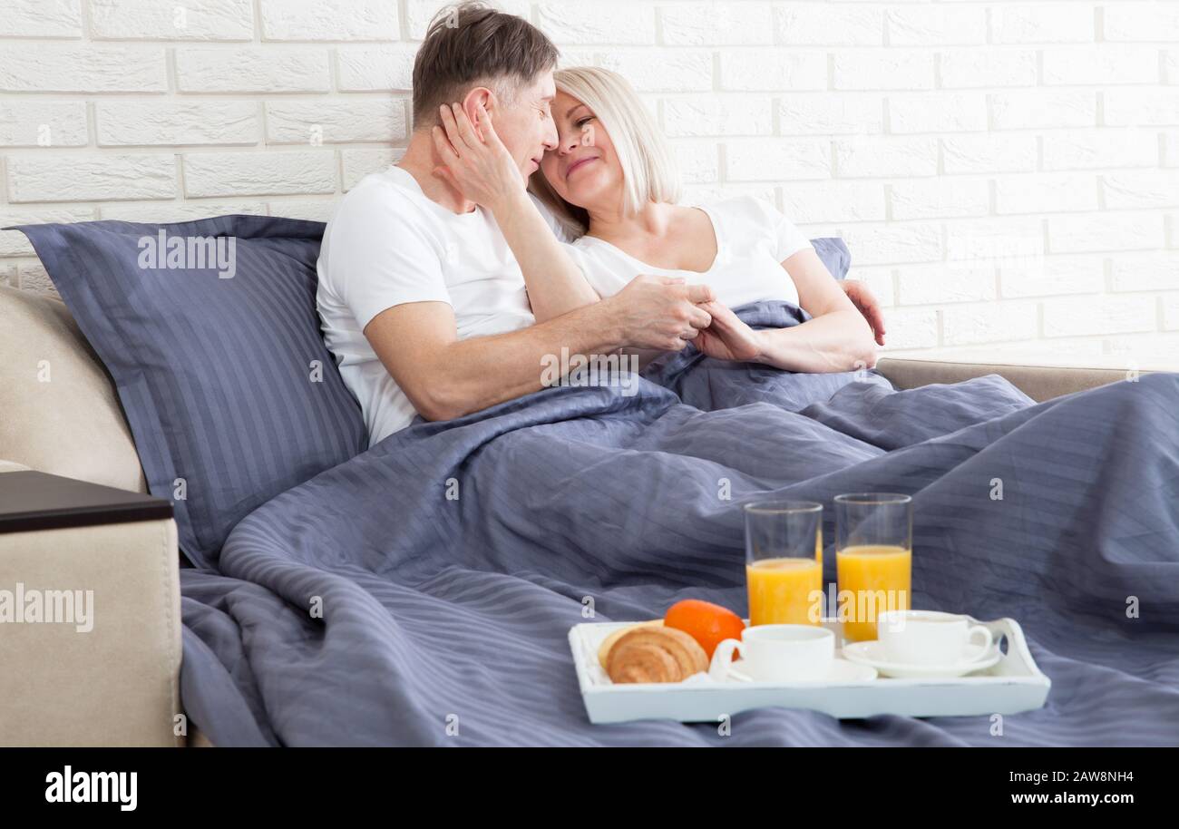 Happy middle aged couple having a breakfast in the bed at hotel Stock Photo
