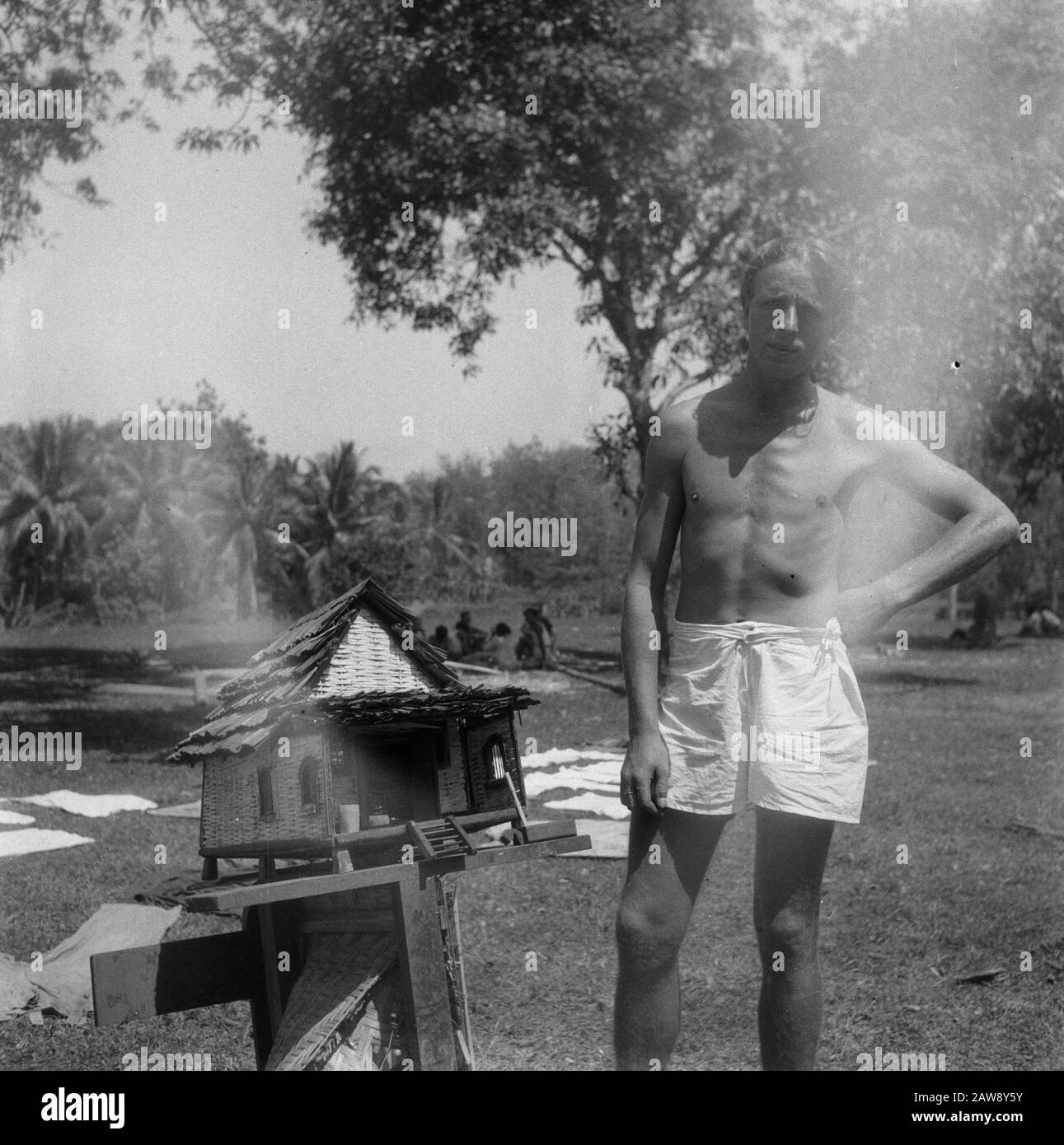 [Man in shorts posing with a model of a bamboo hut Date: 01/01/1947 Location: Indonesia Dutch East Indies Stock Photo