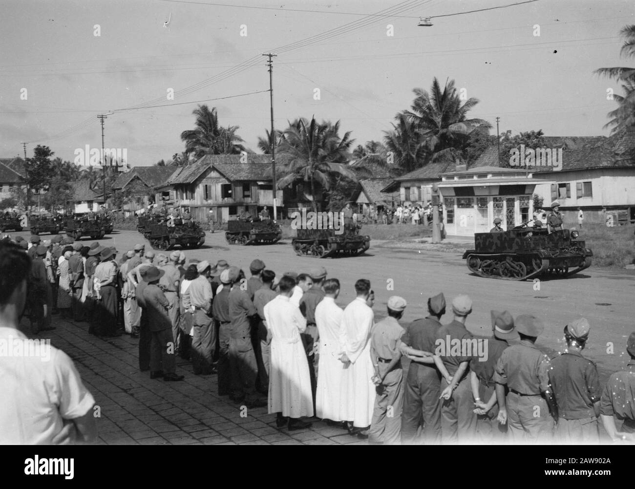 [Military parade in the village. Many people in military uniform look to. Bren Carriers pass] Annotation: In some men along the way, the sleeve logo KNIL brigade Bali-Lombok, battalion Gajah Merah visible Date: 01/01/1947 Location: Indonesia Dutch East Indies Stock Photo