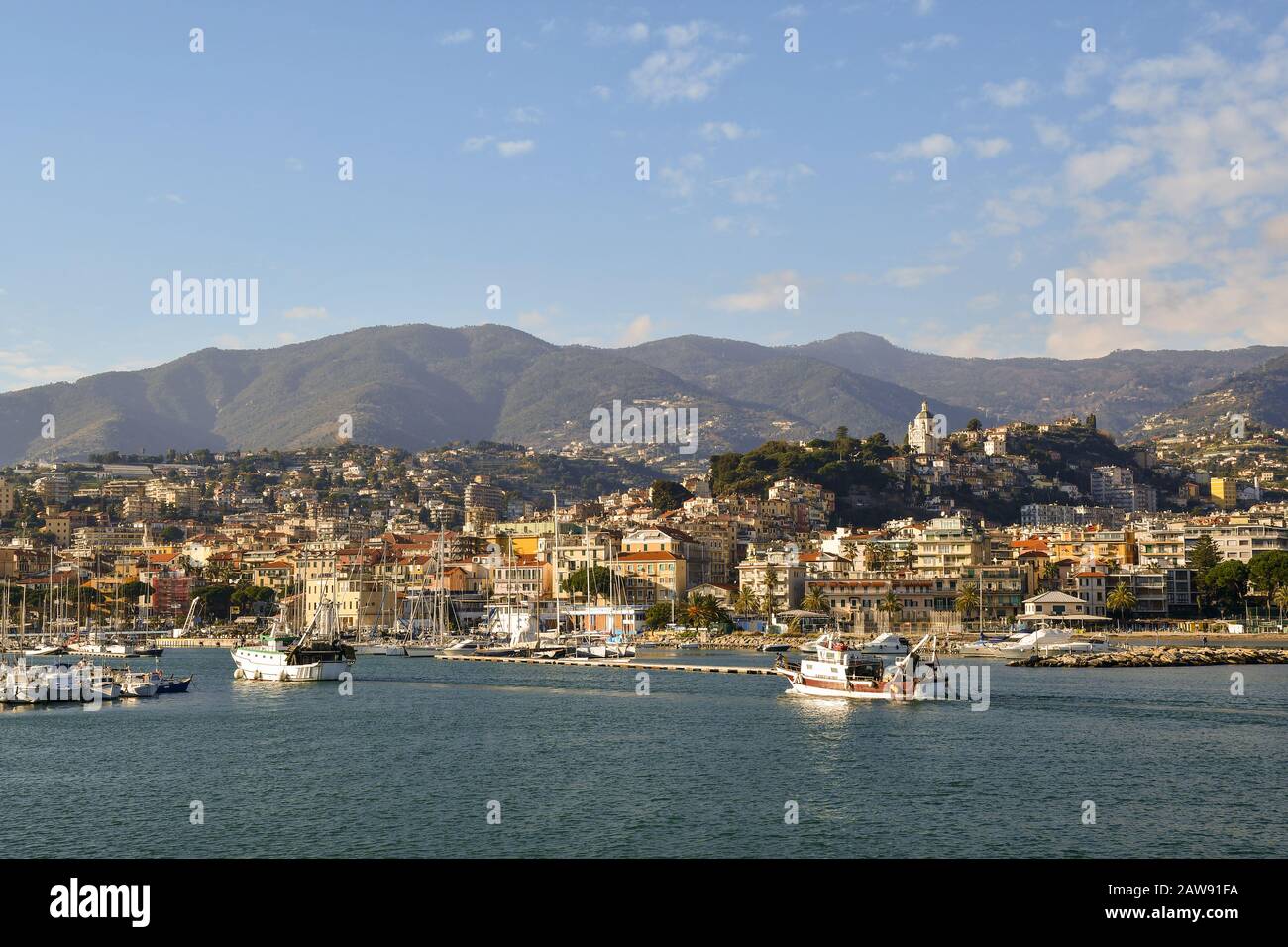 Scenic view of the Old Port of Sanremo with fishing boats and the coastal city with the Ligurian Apennines in background, Sanremo, Liguria, Italy Stock Photo