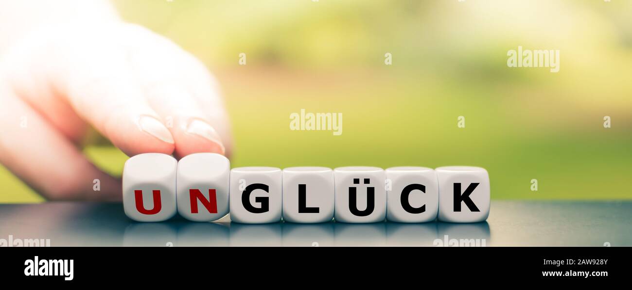 Hand turns dice and changes the German word 'Unglück' ('bad luck') to 'Glück' ('luck'). Stock Photo