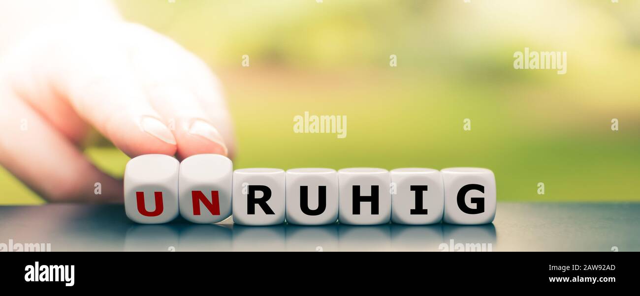 Hand turns dice and changes the German word 'unruhig' ('twitchy') to 'ruhig' ('calm'). Stock Photo