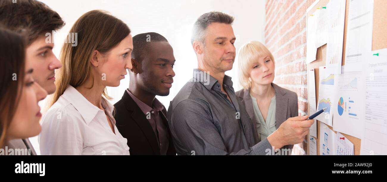 Manager Analyzing The Graph With His Co-workers Attached On Bulletin Board Stock Photo