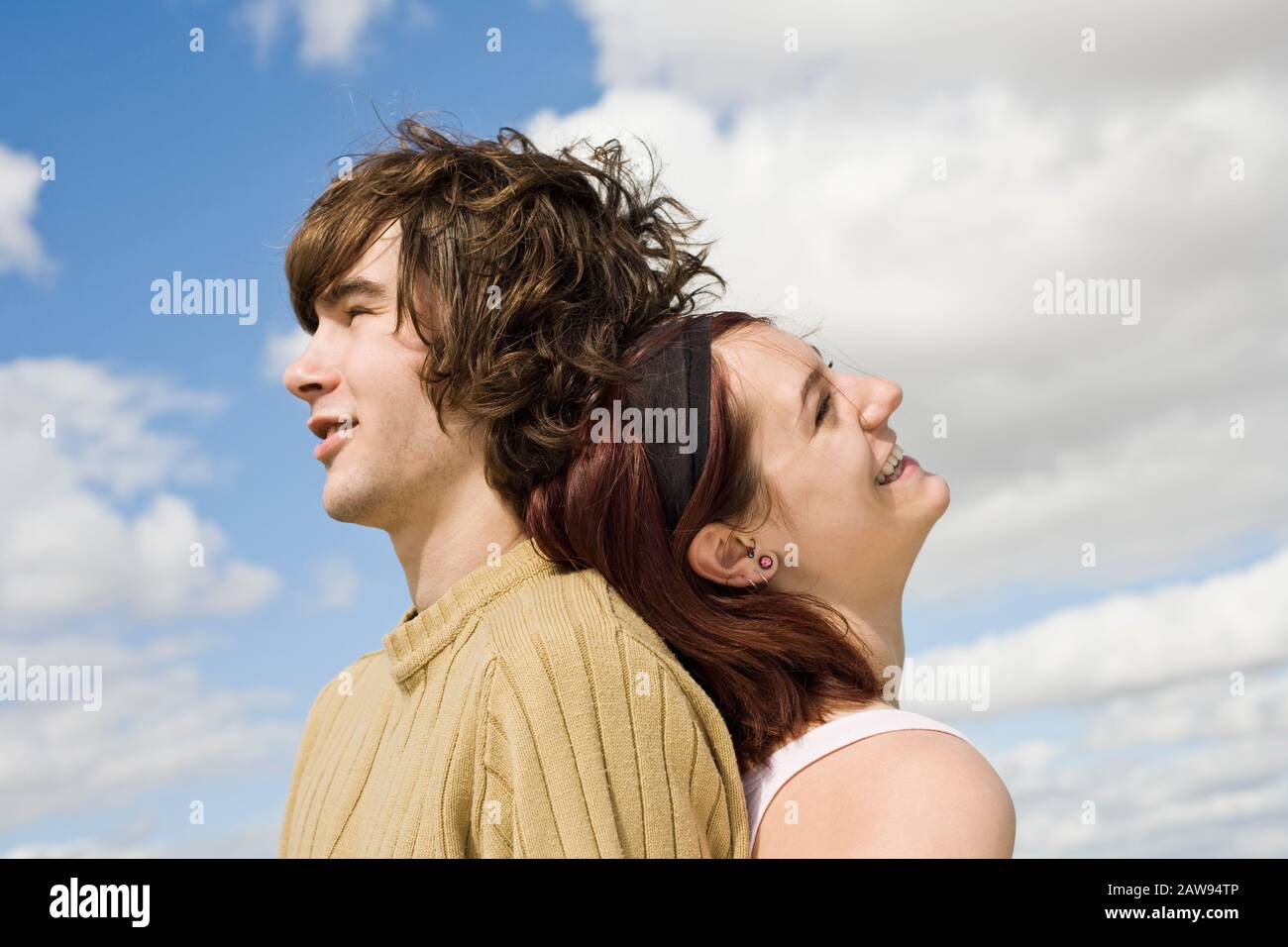 A teenage couple laughing and smiling back to back outdoors Stock Photo