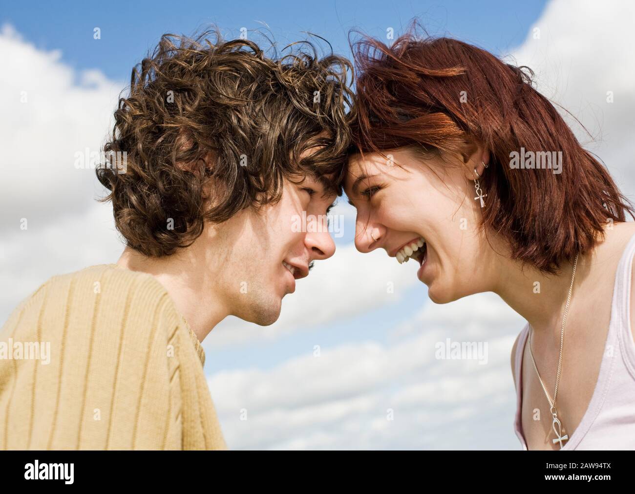 A teenage couple laughing and smiling with their heads together outdoors Stock Photo