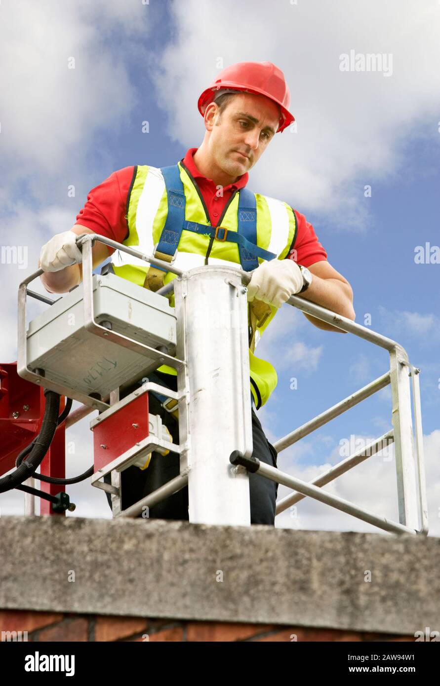 Workman in a cherry picker wearing safety clothing and inspecting a roof Stock Photo