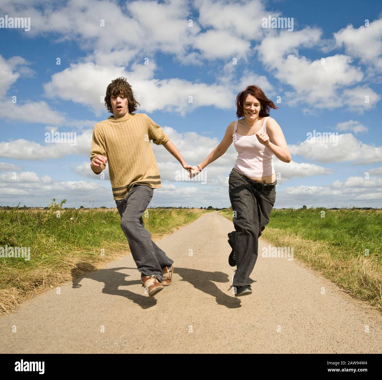 A teenage couple holding hands and running down a country lane towards the camera Stock Photo