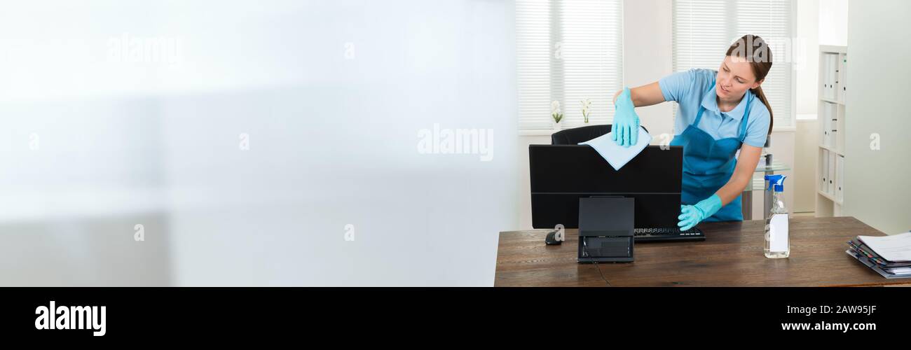 Young Female Maid Cleaning Glass Desk With Feather Duster In Office