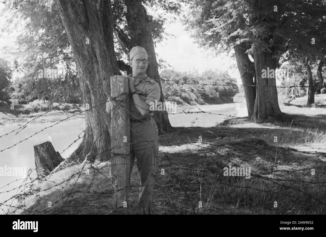 Soldier with glasses and slightly pained look behind a pole with barbed wire Date: 01/01/1947 Location: Indonesia Dutch East Indies Stock Photo