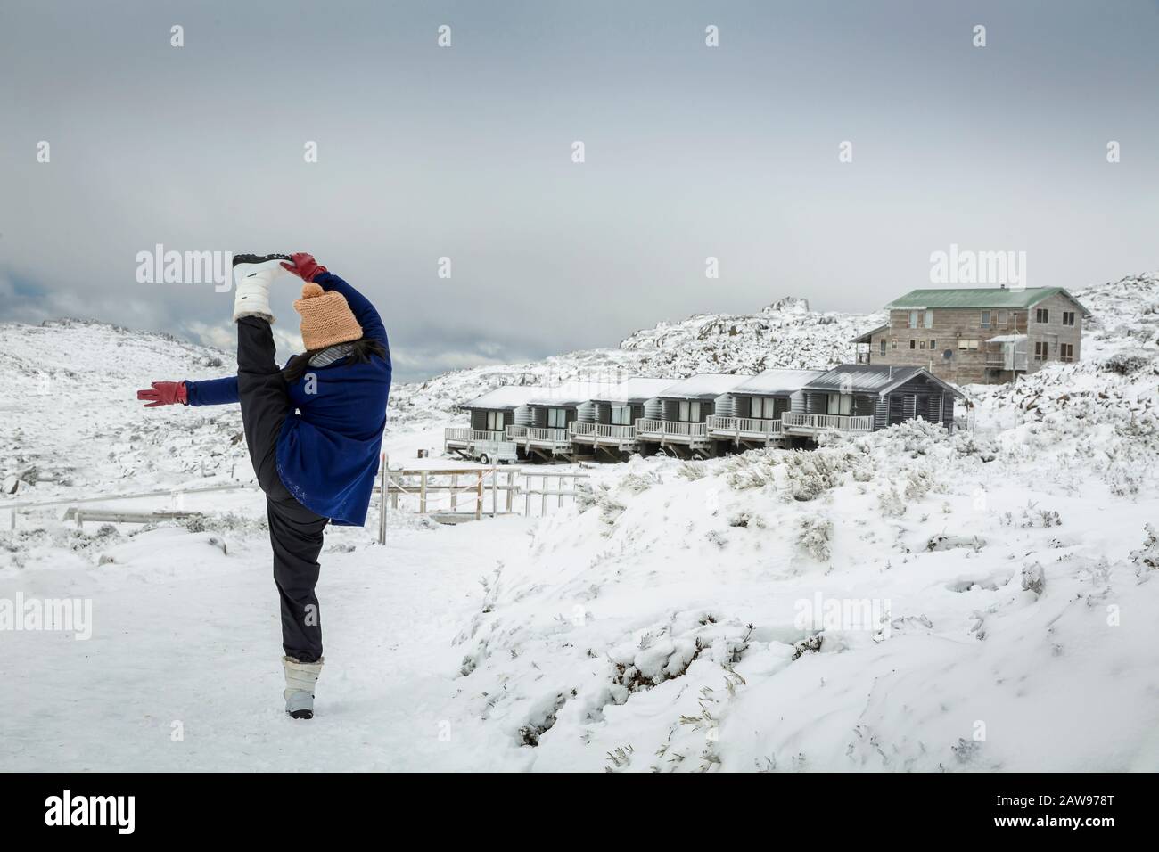 Female doing a standing yoga splits pose in the snow, with Ben Lomond ski resort background, Tasmania, Australia Stock Photo