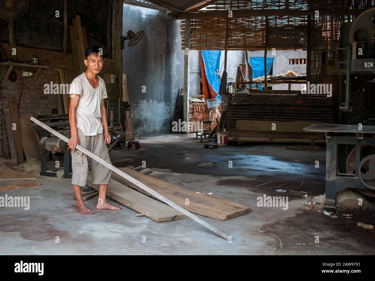Vietnamese carpenter man holding a piece of wood in his carpentry workshop Stock Photo