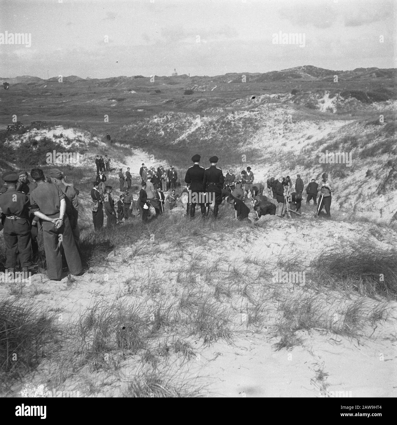 Mass Grave to Waalsdorp  Mass Grave to Waalsdorp. German war criminals and Dutch collaborators give evidence where victims of their crimes are buried and do yourself excavating. Dutch police monitors. Canadian soldiers watch Date: August 1945 Location: Waalsdorp, South Holland Keywords: mass graves, ruins, World War II Stock Photo