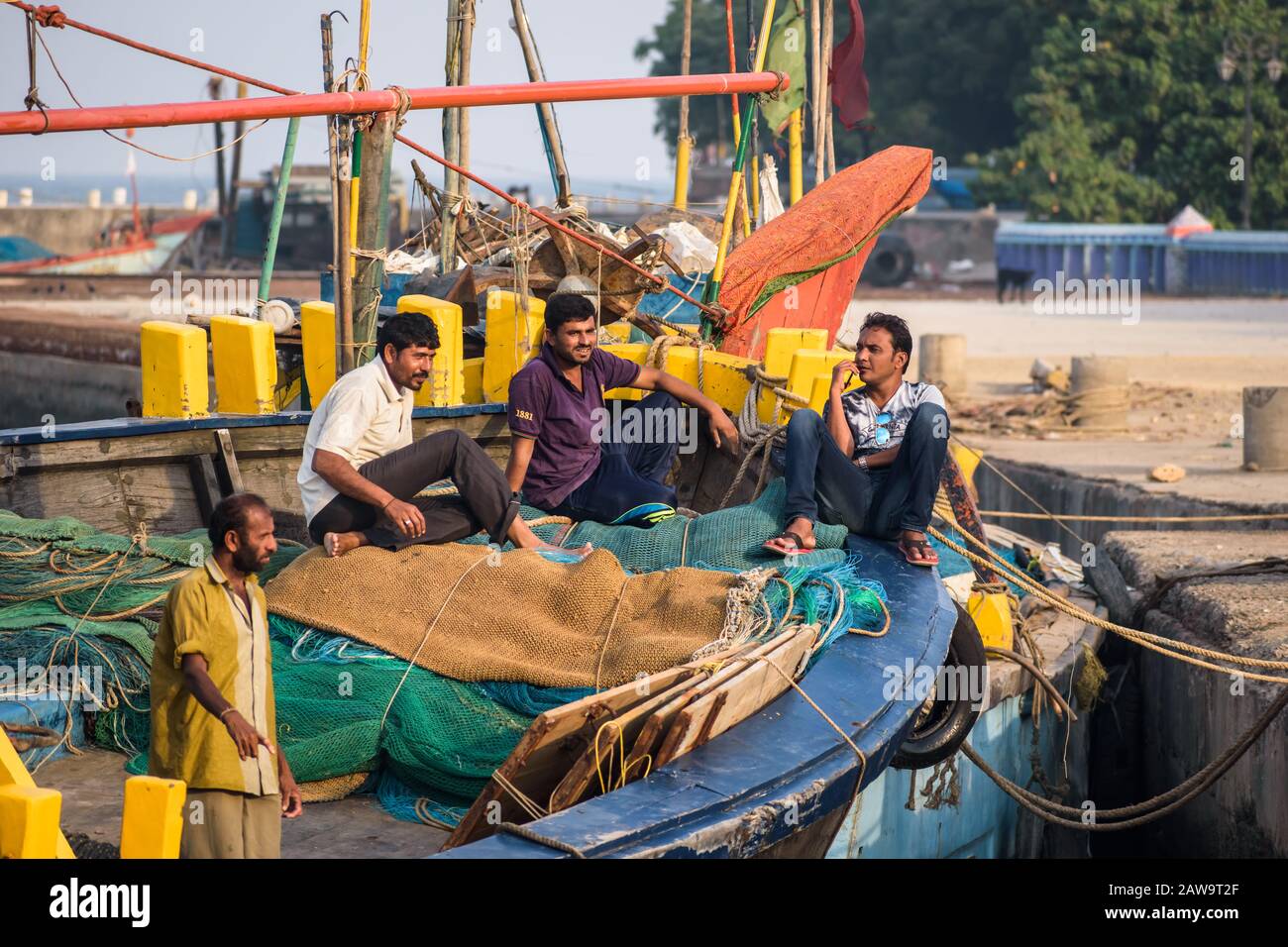 Diu, India - December 2018: Fishermen idle and chat on a colorful boat by the pier in the island of Diu. Stock Photo