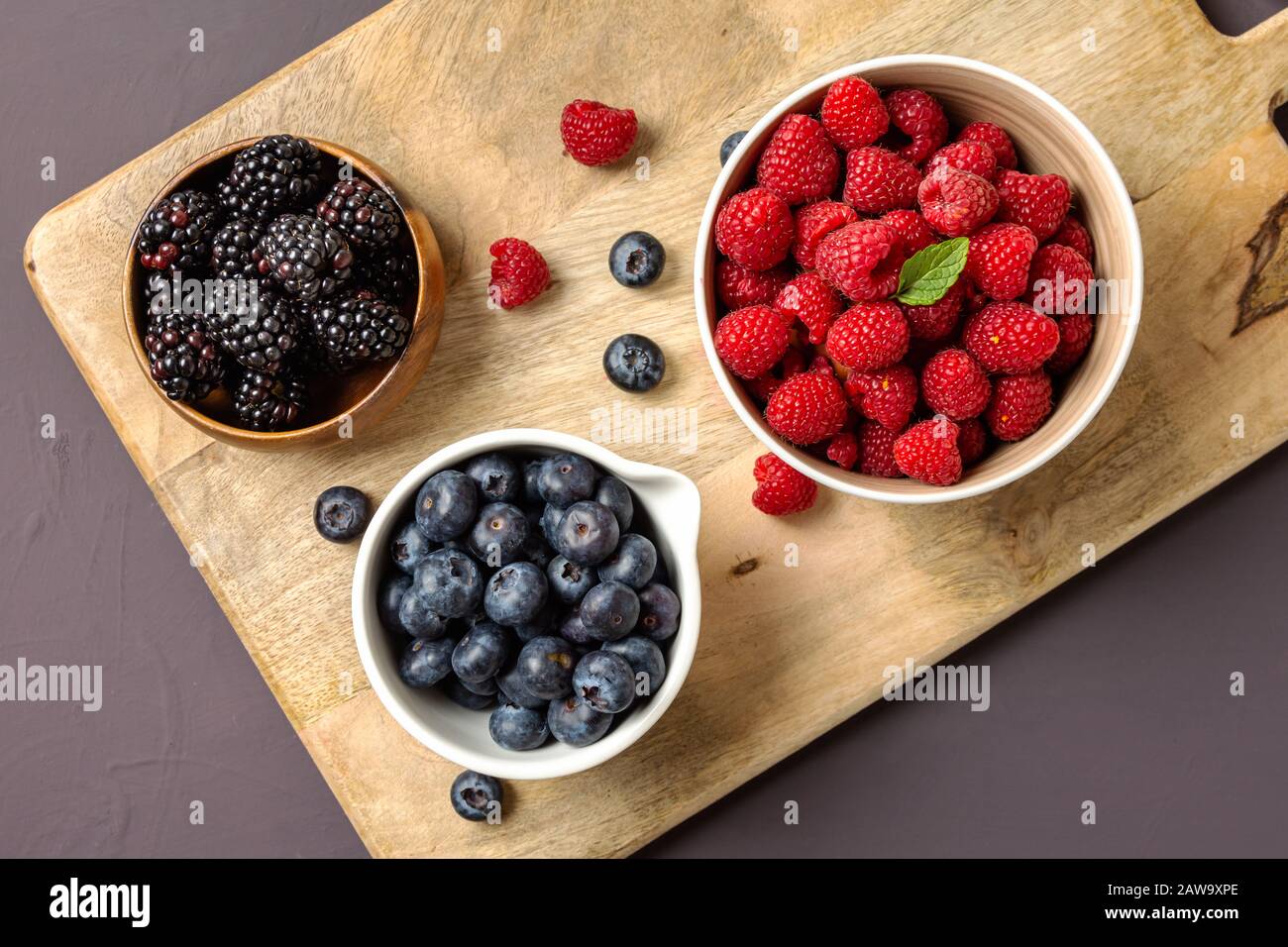 three bowls with wild berries, raspberry, blueberries, blackberries, on rustic wooden background Stock Photo