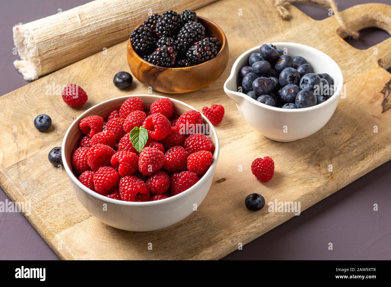 three bowls with wild berries, raspberry, blueberries, blackberries, on rustic wooden background Stock Photo