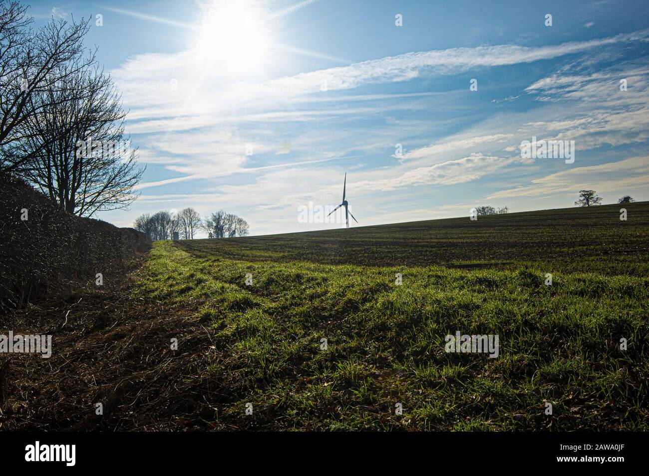 Ploughed fields in winter, with distant wind turbine and dew drenched grass in foreground Stock Photo