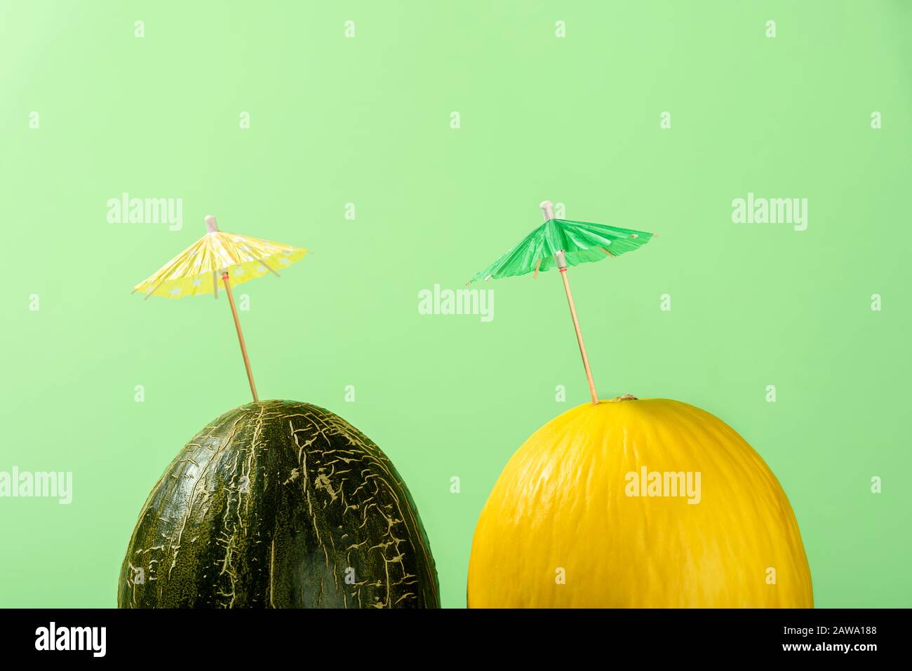 Yellow and green melons with cocktail umbrella on green background in