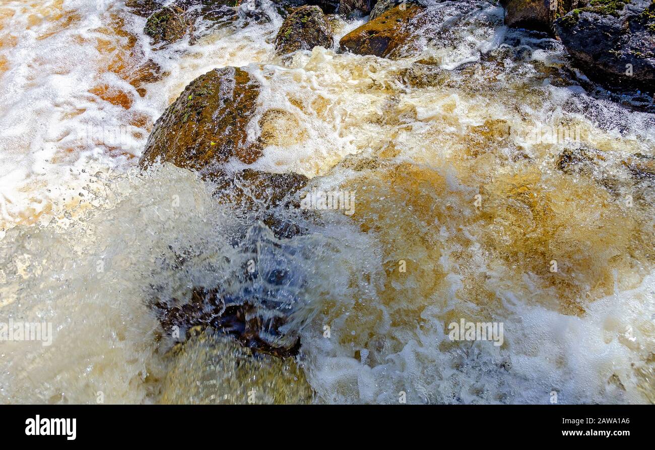 foaming and splashing gold coloured white water overflowing rocks in Sweden Stock Photo