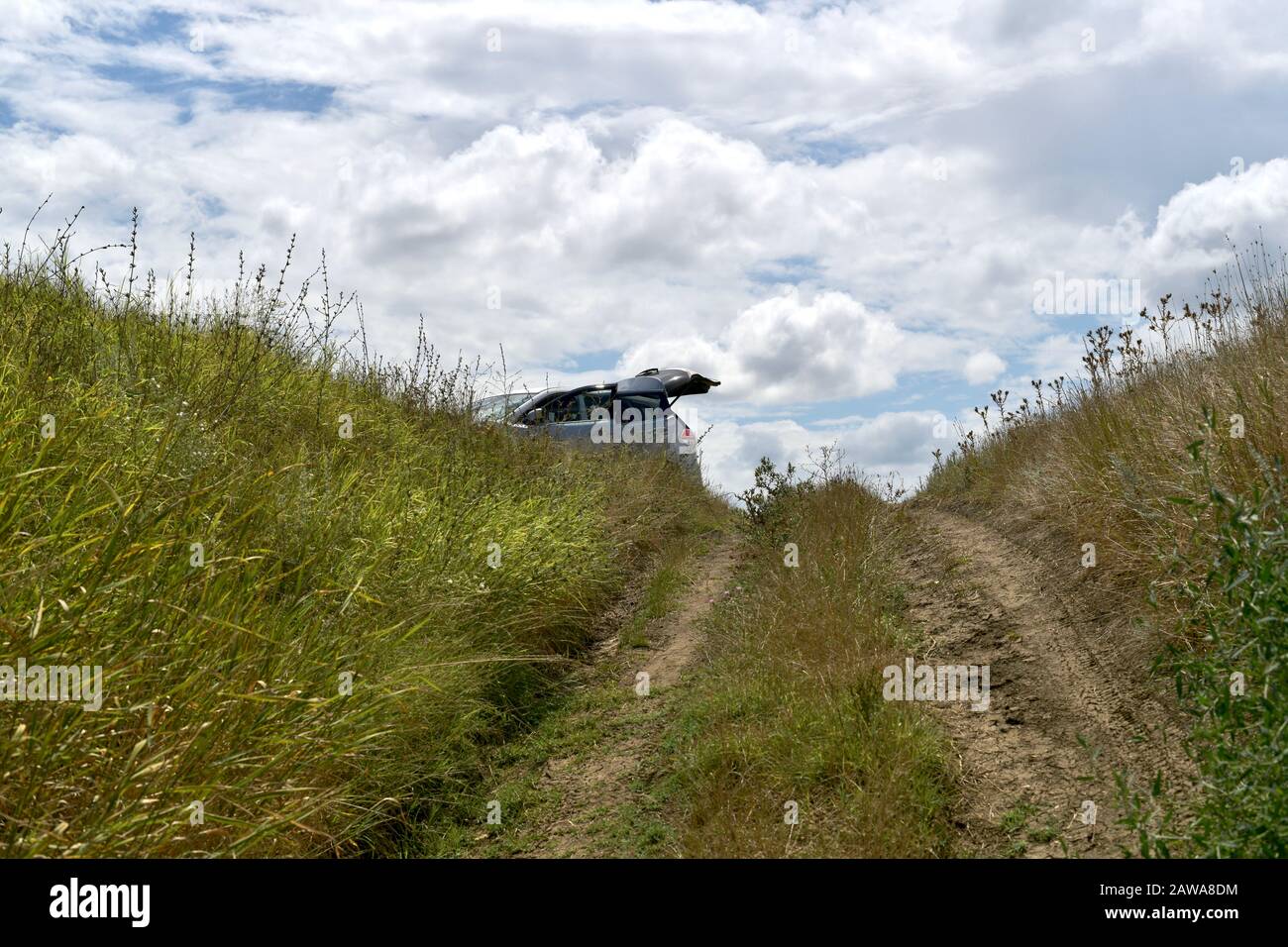 The dirt road leading up to the car is partially visible with an open raised trunk on a hill among the steppe grasses. Stock Photo