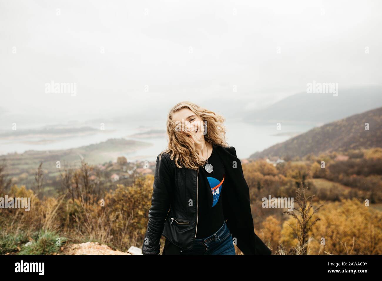 happy girl with curly blond hair dances on a lake alone, her hair is flying because of the wind flow, free as a bird. photo of girl with curly hair Stock Photo