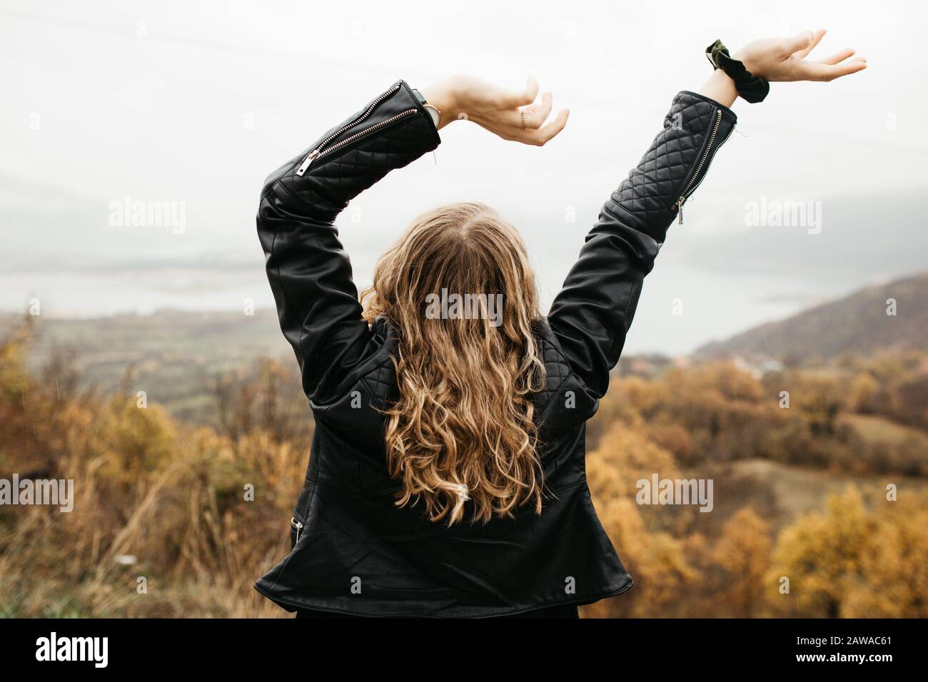 happy girl with curly blond hair dances on a lake alone, her hair is flying because of the wind flow, free as a bird. photo of girl with curly hair Stock Photo