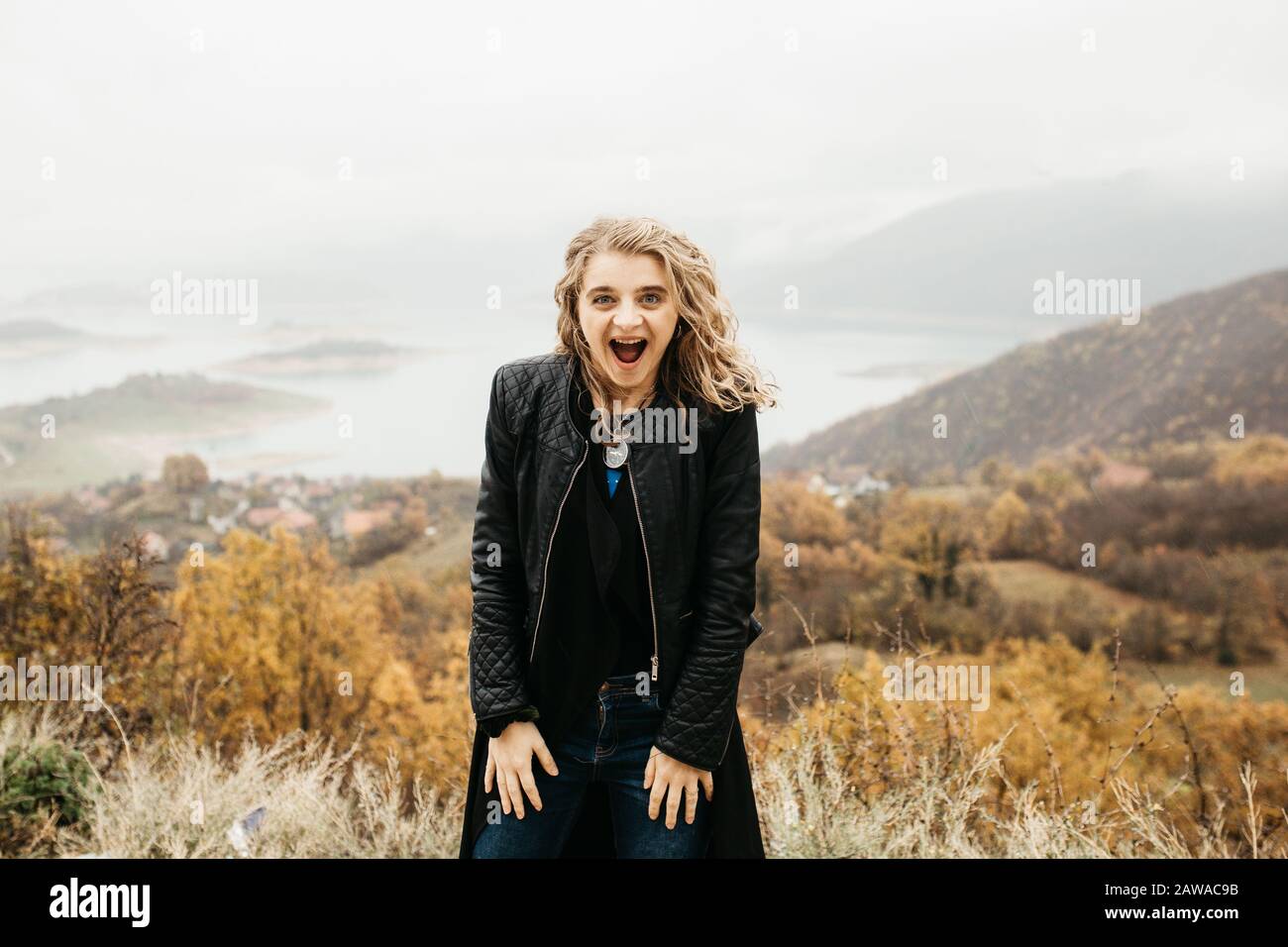 happy girl with curly blond hair dances on a lake alone, her hair is flying because of the wind flow, free as a bird. photo of girl with curly hair Stock Photo