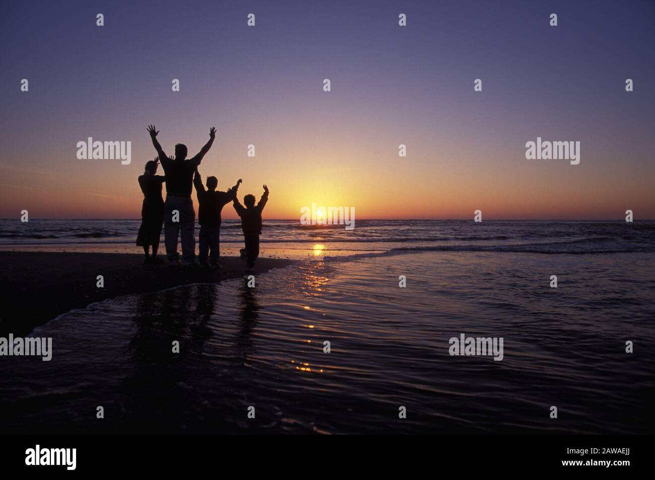 Silhouette of a family on the beach in North Carolina raising their hands to the sunrise Stock Photo