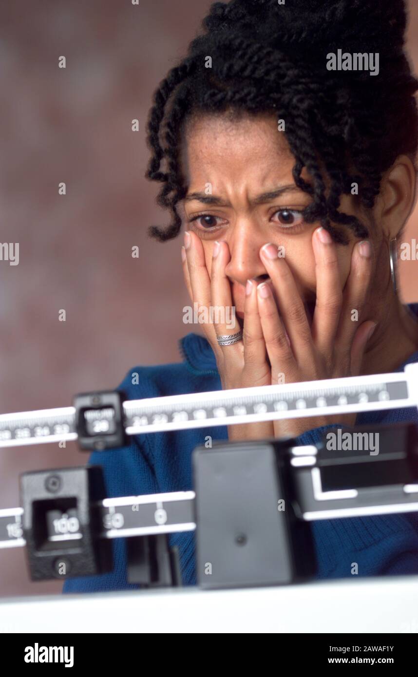 An African-American woman is shocked looking at her weight on a doctor scale after dieting Stock Photo