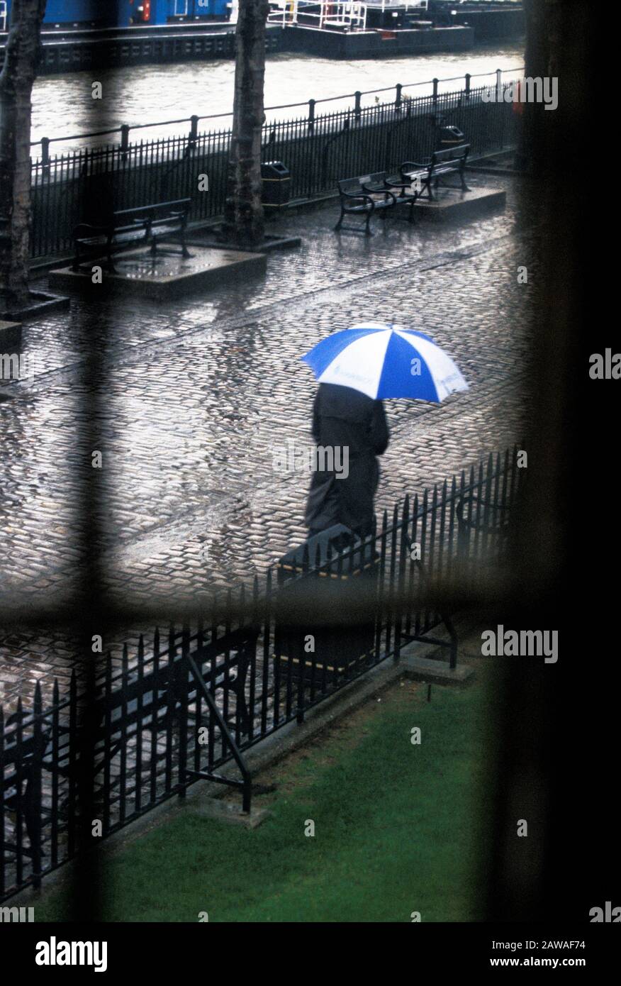 Man with umbrella walks along the Thames on a rainy London morning Stock Photo