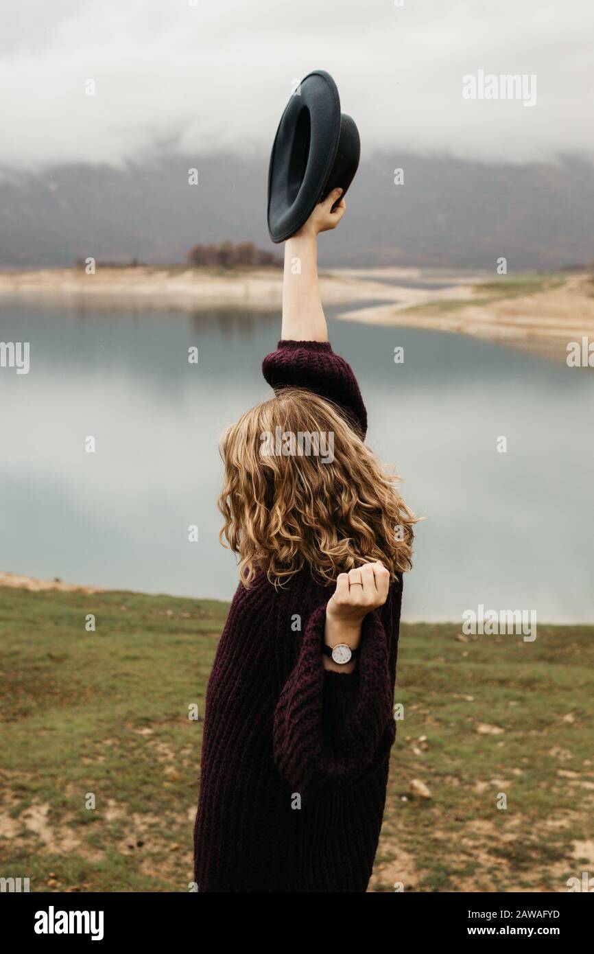 beautiful woman in purple sweater holding her hat and enjoying trip on the lake. Female tourist exploring lake. She is smiling and catching her hat. Stock Photo