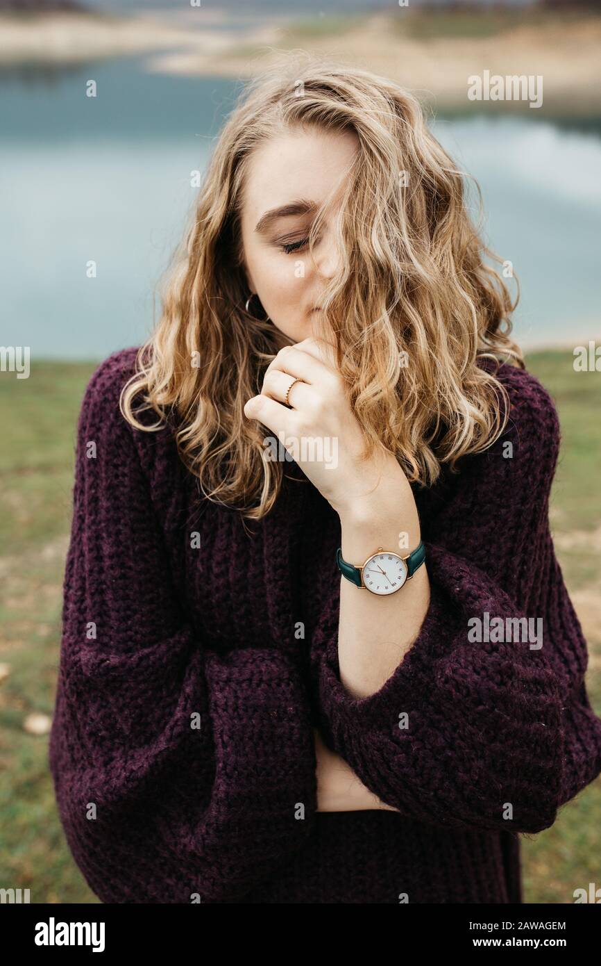 Outdoors portrait of young woman with curly hair wearing fashionable wrist watch. She is standing near lake. Stock Photo