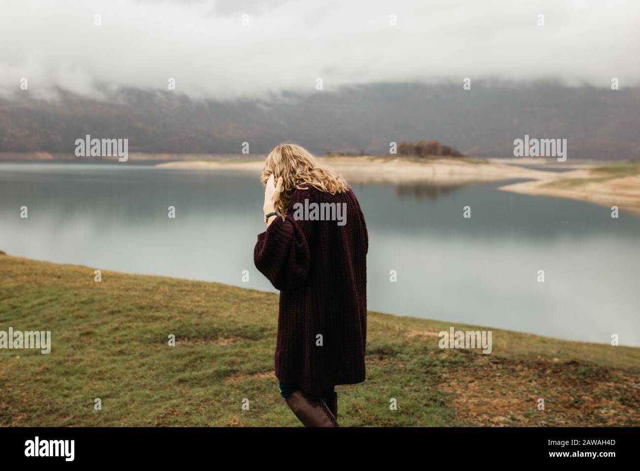 Outdoors portrait of young woman with curly hair wearing fashionable wrist watch. She is standing near lake. Stock Photo