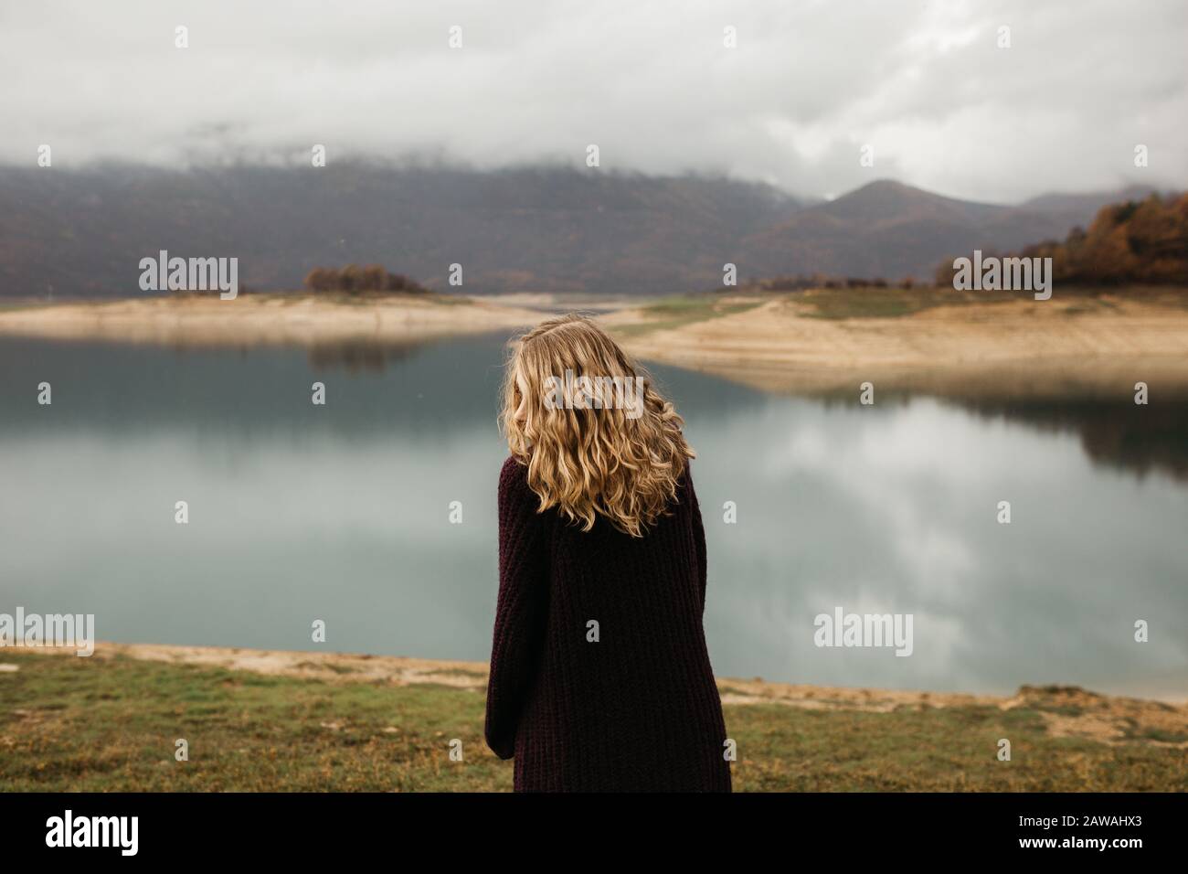 happy girl with curly blond hair dances on a lake alone, her hair is flying because of the wind flow, free as a bird. photo of girl with curly hair st Stock Photo