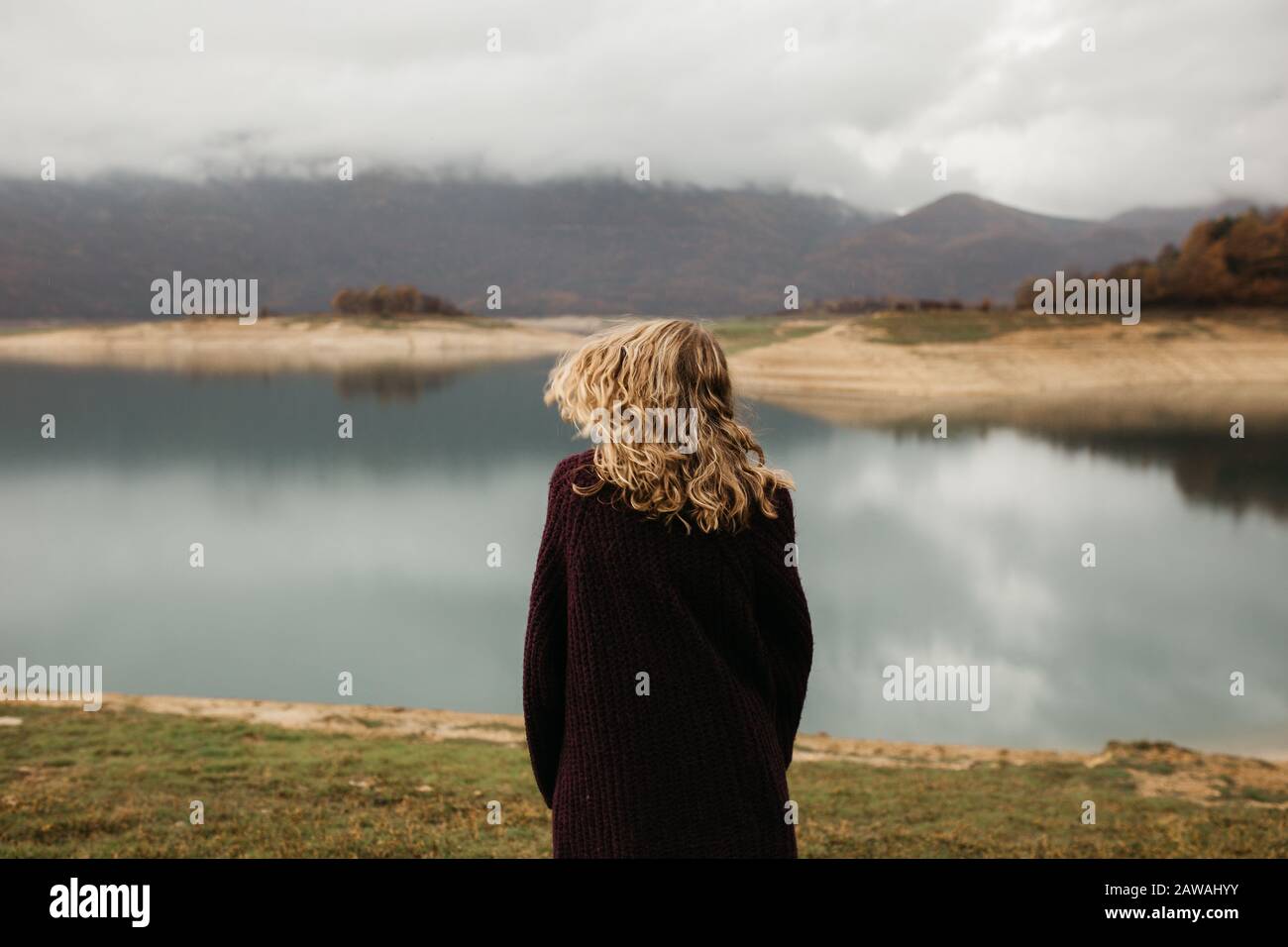 happy girl with curly blond hair dances on a lake alone, her hair is flying because of the wind flow, free as a bird. photo of girl with curly hair st Stock Photo