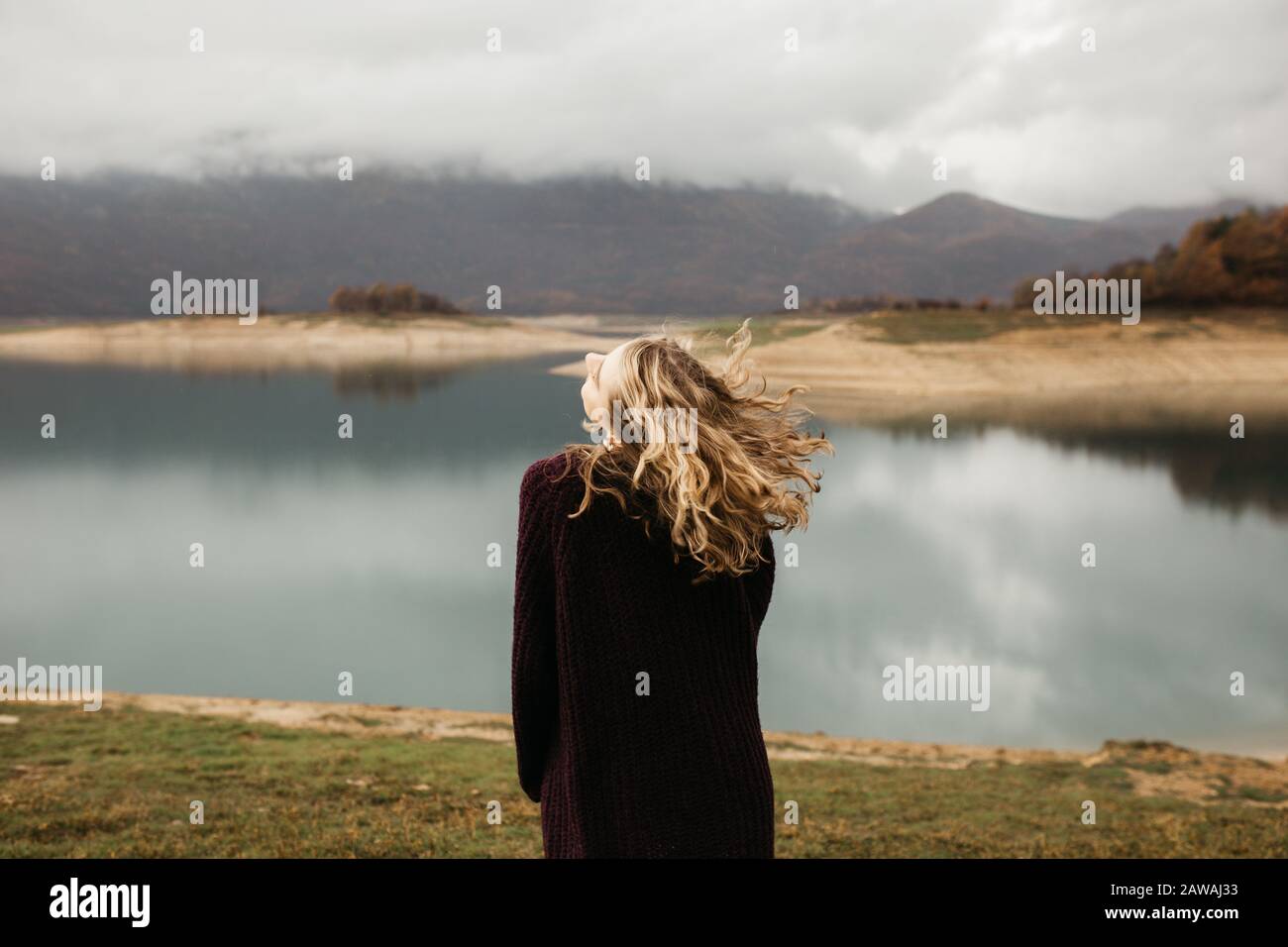 happy girl with curly blond hair dances on a lake alone, her hair is flying because of the wind flow, free as a bird. photo of girl with curly hair st Stock Photo