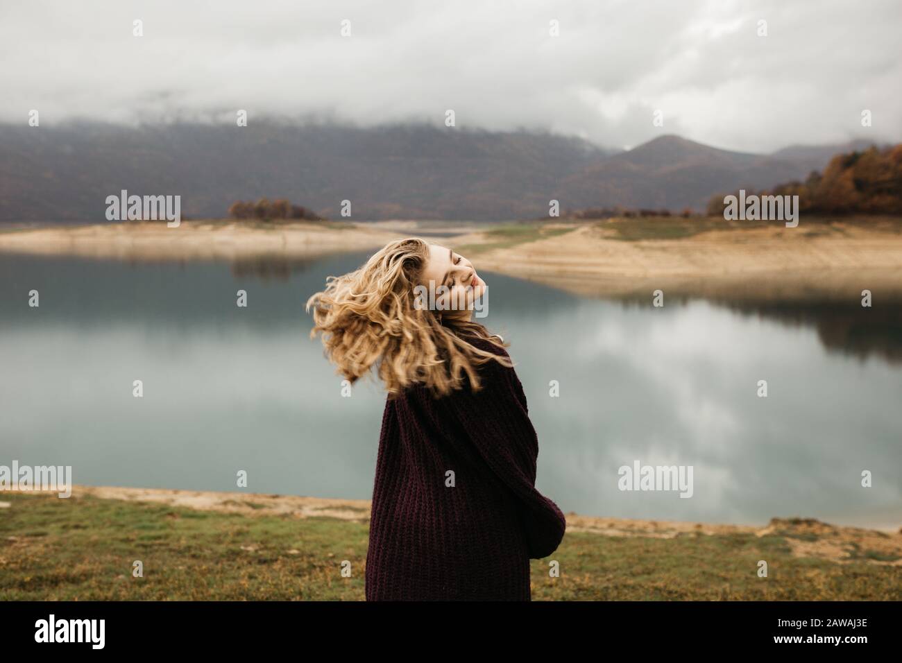 happy girl with curly blond hair dances on a lake alone, her hair is flying because of the wind flow, free as a bird. photo of girl with curly hair st Stock Photo