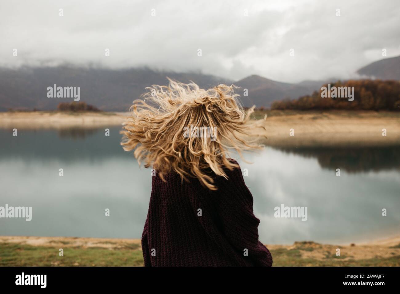 happy girl with curly blond hair dances on a lake alone, her hair is flying because of the wind flow, free as a bird. photo of girl with curly hair st Stock Photo