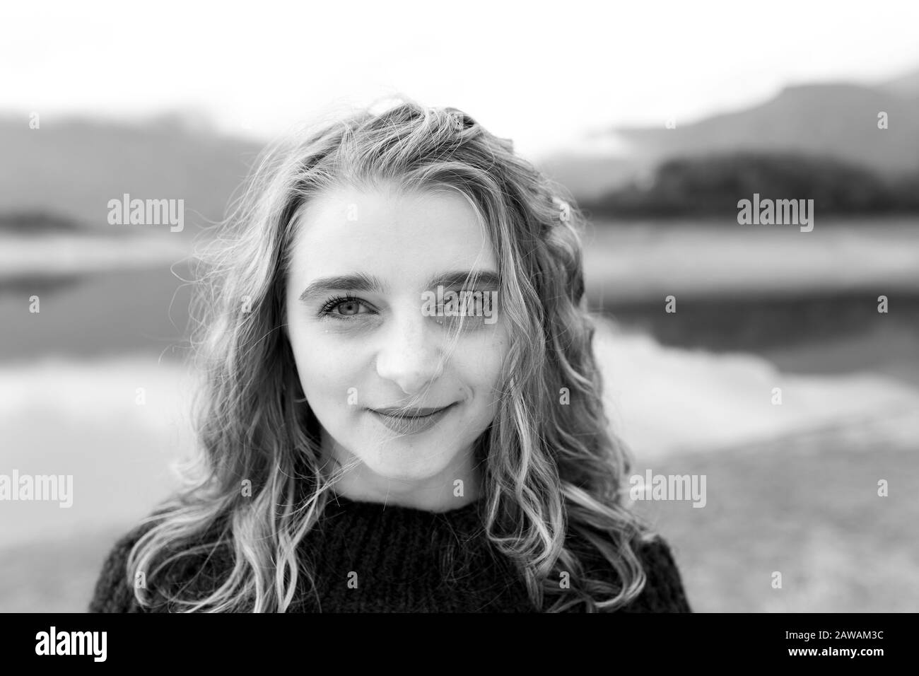 Outdoors portrait of young woman with curly hair wearing fashionable wrist watch. She is standing near lake. Stock Photo