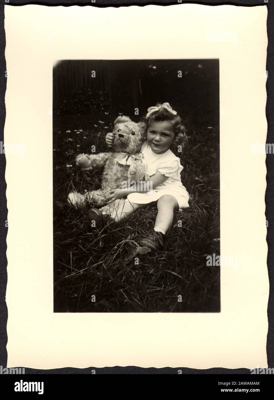 1930's , GERMANY : Little girl with a Teddy Bear , seated in grass ...
