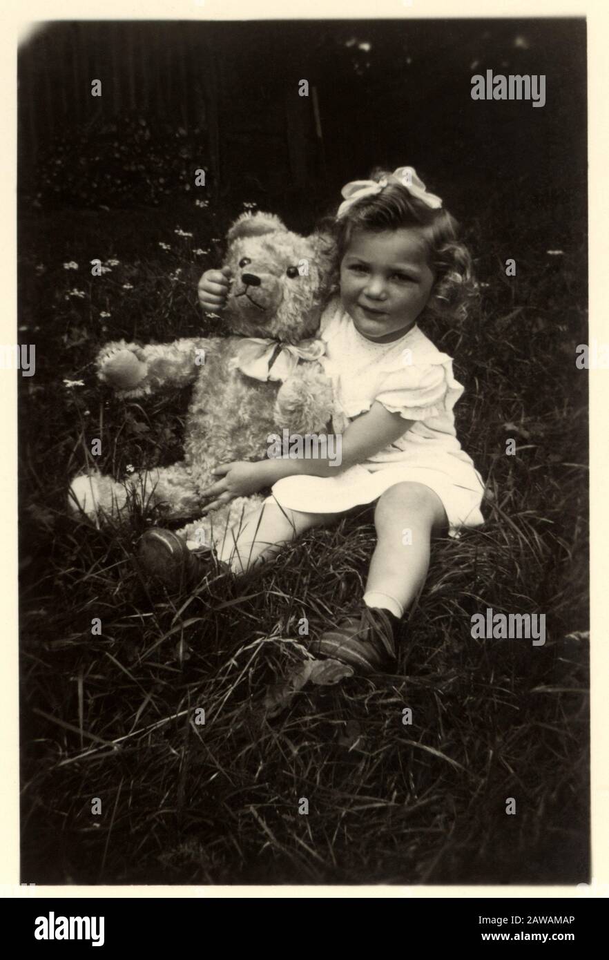 1930's , GERMANY : Little girl with a Teddy Bear , seated in grass ...