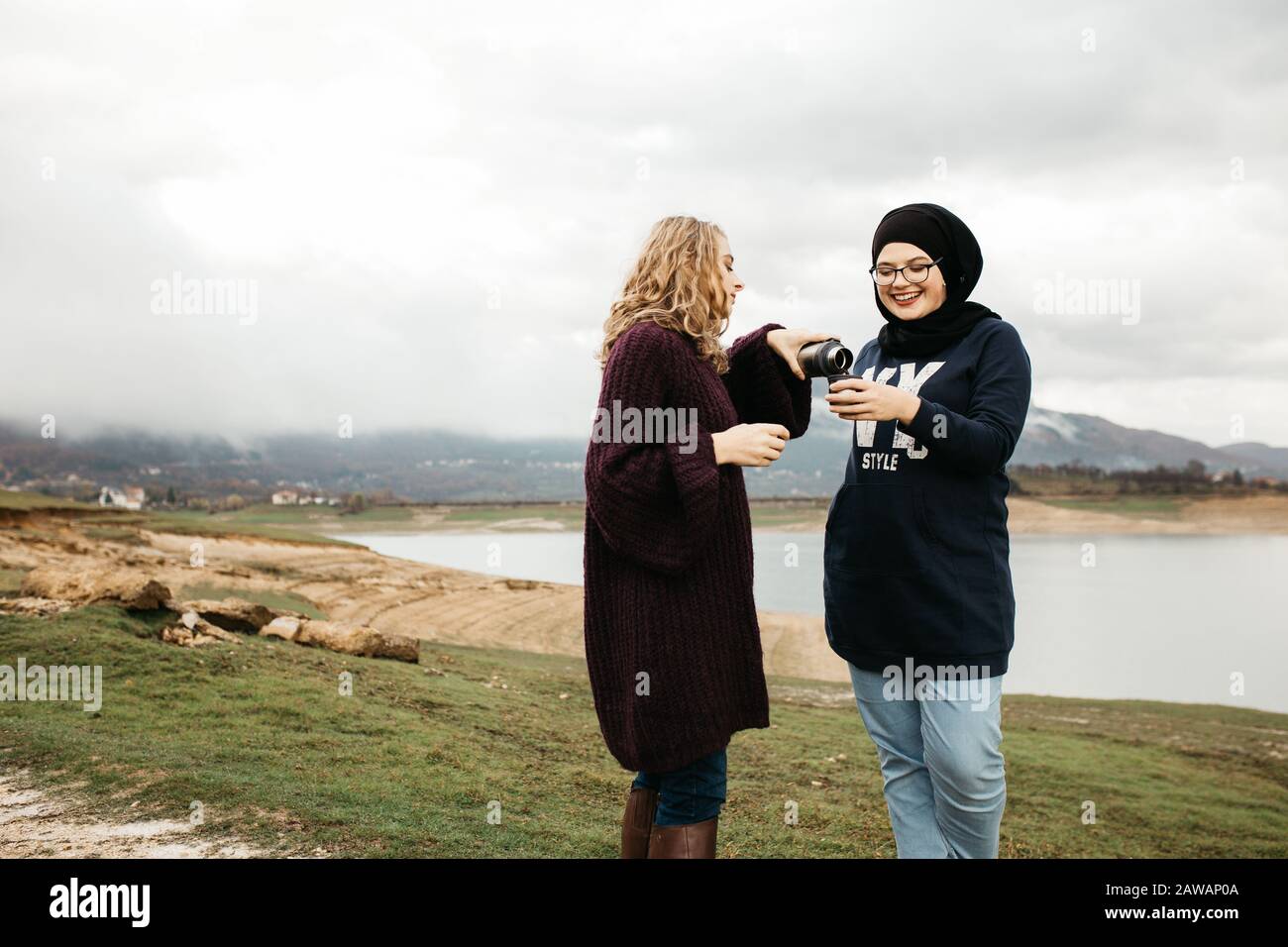 Lifestyle portrait of two best friends, smiling and drinking coffee together. Outdoor photo of two young women, one with hijab, enjoying each other co Stock Photo