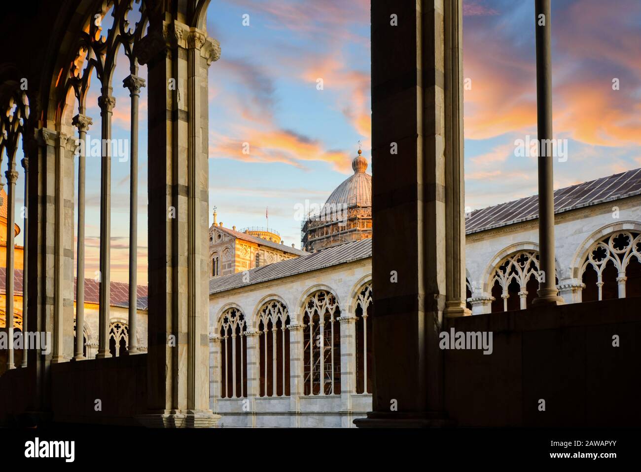 The Duomo Pisa Cathedral dome is visible under a colorful sunset from inside stone arched windows in the Tuscan city of Pisa, Italy. Stock Photo