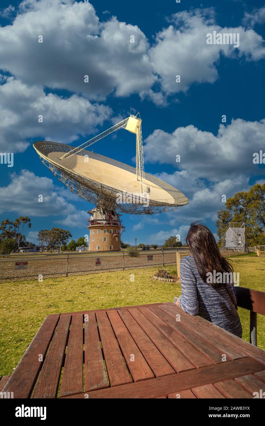 Female tourist seated at a table looking up at the Parkes Radio Telescope know as 'The Dish' that is pointed skyward in New South Wales, Australia. Stock Photo