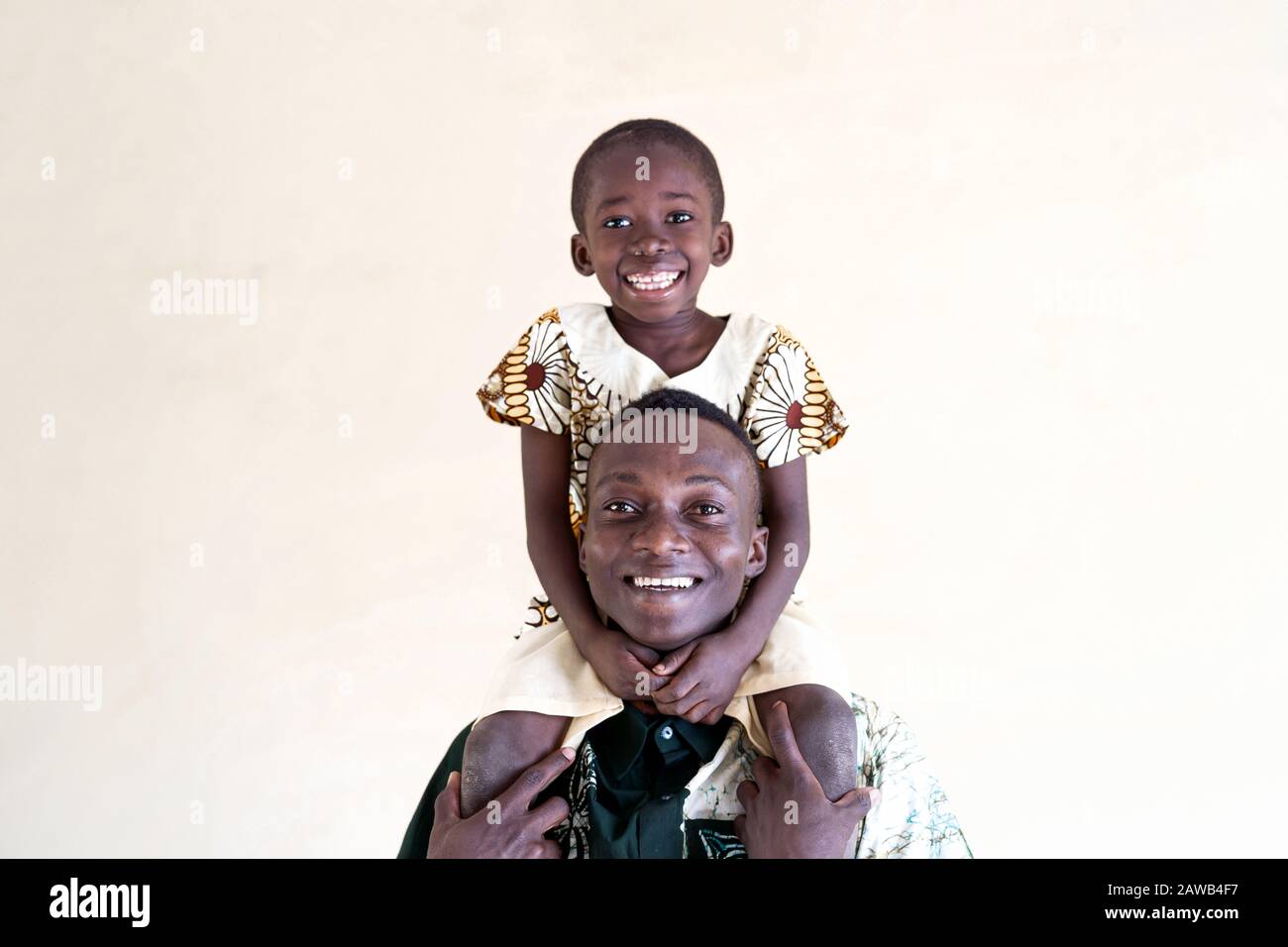 Cute dad and son of African ethnicity descent laughing and smiling for the photo in front of isolated yellowish background Stock Photo